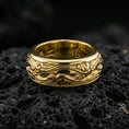 Load image into Gallery viewer, Gold plated scrollwave spinner band ring on volcanic rock, detailed flowing wave filigree on rotating band, luxury jewelry product photography.