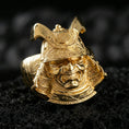 Load image into Gallery viewer, Sterling silver samurai armor ring with a gold plated finish, detailed kabuto helmet crest and demon-like warrior expression, macro product shot on volcanic rock
