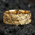 Load image into Gallery viewer, Gold plated oni mask band ring on volcanic rock, detailed Japanese demon face relief with ornamental cloud patterns, luxury jewelry product photography.
