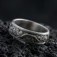Load image into Gallery viewer, Oxidized sterling silver tree branch band ring on dark volcanic rock, detailed root and leaf vine engraving with woodland texture, premium macro product shot.