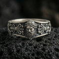 Load image into Gallery viewer, Oxidized sterling silver Zeus portrait band ring on dark volcanic rock, high-relief bearded god face with ornate classical scroll panels, premium macro product shot.