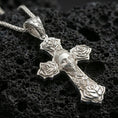 Load image into Gallery viewer, Polished silver Chicano style cross pendant with sculpted roses and central masked portrait placed on textured volcanic rock in a premium studio composition