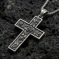 Load image into Gallery viewer, Oxidized rose cross pendant with engraved floral details displayed on dark volcanic rock in a close-up luxury jewelry composition