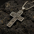 Load image into Gallery viewer, Bronze rose cross pendant with engraved floral details displayed on dark volcanic rock in a close-up luxury jewelry composition