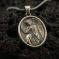 Load image into Gallery viewer, Bronze angel pendant with oval frame and detailed winged figure displayed on dark volcanic rock in a close-up luxury jewelry composition