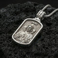 Load image into Gallery viewer, Polished silver Jesus Sacred Heart pendant with engraved halo, INRI inscription, and rounded rectangular frame placed on textured volcanic rock in a premium studio product shot
