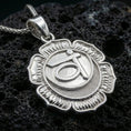 Load image into Gallery viewer, Polished silver chakra necklace with layered lotus design, circular center, and engraved throat chakra symbol placed on textured volcanic rock in a premium studio product shot