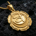 Load image into Gallery viewer, Gold plated throat chakra medallion pendant with lotus petal border and raised spiritual symbol showcased on black volcanic rock in a refined macro jewelry image