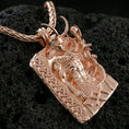 Load image into Gallery viewer, Rose gold plated Loki pendant necklace on textured volcanic rock, centered studio-style close-up with soft rosy glow on the horned portrait and intricate knotwork frame.