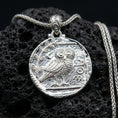 Load image into Gallery viewer, Polished silver owl coin pendant necklace on textured volcanic rock, crisp macro product photo emphasizing clean edges, sharp feather engraving, and bright reflective highlights.