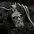 Load image into Gallery viewer, Oxidized Odin pendant necklace on textured volcanic rock, centered close-up highlighting the one-eyed helmeted face, braided beard, and deep antique shadowed contrast.