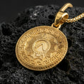 Load image into Gallery viewer, Gold plated Spartan shield medallion pendant necklace on textured volcanic rock, premium close-up with warm reflective shine across the Greek meander frame and raised shield emblem.