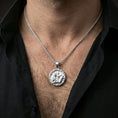 Load image into Gallery viewer, Polished silver Odin and raven medallion pendant necklace worn on the neck, clean lifestyle wear shot capturing bright shine and the detailed raven-and-spear relief in natural light.