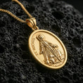 Load image into Gallery viewer, Gold plated Saint Rochus medal with detailed saint portrait, walking staff, and loyal dog motif showcased on black volcanic rock in a refined macro jewelry image