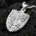 Load image into Gallery viewer, Polished silver Saint Michael pendant with angel warrior relief, shield frame, sword, and raised wing details placed on textured volcanic rock in a premium studio product shot