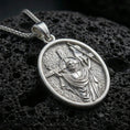 Load image into Gallery viewer, Polished silver religious oval pendant with resurrected Jesus figure, victory banner, and cross motif placed on textured volcanic rock in a premium studio product shot