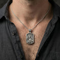 Load image into Gallery viewer, Oxidized Saint Gabriel pendant with angel figure and cross staff worn on the neck in a lifestyle jewelry shot, styled against the chest for a devotional and timeless look