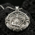 Load image into Gallery viewer, Polished silver Archangel Raphael medallion with round ornamental frame, detailed angel relief, and sacred healing symbol placed on textured volcanic rock in a premium studio product shot