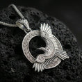 Load image into Gallery viewer, Polished silver Celtic raven knotwork pendant necklace on textured volcanic rock, crisp macro product photo emphasizing clean edges, sharp feather lines, and detailed Celtic weave engraving.