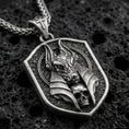 Load image into Gallery viewer, Oxidized Anubis pendant necklace on textured volcanic rock, centered close-up highlighting the jackal god head, halo-like frame, skull detail, and deep antique shadowed contrast.