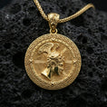 Load image into Gallery viewer, Gold plated Perseus coin pendant necklace on textured volcanic rock, premium close-up with warm reflective shine across the winged helmet, facial relief, and raised meander frame.