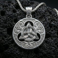 Load image into Gallery viewer, Polished silver Celtic triquetra pendant necklace on textured volcanic rock, crisp macro product photo emphasizing clean edges, sharp knotwork relief, and bright reflective highlights across the circular frame.