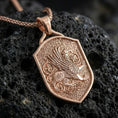 Load image into Gallery viewer, Rose gold plated griffin shield pendant necklace on textured volcanic rock, centered studio-style close-up showcasing soft rosy glow and intricate mythical guardian detailing with a refined finish.