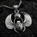 Load image into Gallery viewer, Polished silver winged scarab beetle pendant necklace on textured volcanic rock, crisp macro product photo emphasizing clean edges, sharp feathered wing lines, and bright reflective highlights on the Eye of Ra emblem.