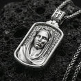 Load image into Gallery viewer, Polished silver Madonna medallion with detailed draped veil, calm facial relief, and framed devotional design placed on textured volcanic rock in a premium studio product shot