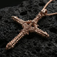 Load image into Gallery viewer, Rose gold plated gothic cross pendant with intricate biomechanical design, sculpted industrial-organic relief, and dramatic elongated form resting on volcanic rock in an elegant close-up product presentation