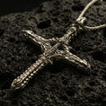 Load image into Gallery viewer, Bronze biomechanical gothic cross pendant with intricate skeletal and machine-like detailing displayed on dark volcanic rock in a close-up luxury jewelry composition