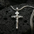 Load image into Gallery viewer, Polished silver Jesus crucifix necklace with detailed corpus relief, INRI plaque, and classic cross silhouette placed on textured volcanic rock in a premium studio product shot