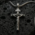 Load image into Gallery viewer, Oxidized INRI crucifix pendant with sculpted Jesus figure and wood-textured cross displayed on dark volcanic rock in a close-up luxury jewelry composition