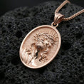 Load image into Gallery viewer, Rose gold plated religious Jesus medal with sacred face relief, crown of thorns, and elongated oval silhouette resting on volcanic rock in an elegant close-up product presentation