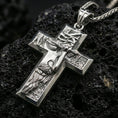 Load image into Gallery viewer, Polished silver Christian cross pendant with detailed Christ figure, bold cross silhouette, and engraved background texture placed on textured volcanic rock in a premium studio product shot