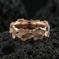 Load image into Gallery viewer, Rose gold plated floral band ring on textured volcanic rock, centered studio-style close-up showcasing soft rosy glow and intricate floral engraving with a refined finish.