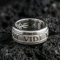 Load image into Gallery viewer, Polished silver Veni Vidi Vici spinner ring on textured volcanic rock, crisp macro product photo emphasizing clean edges, sharp engraved text, and bright reflective highlights on the spinning center.