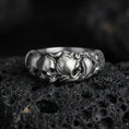 Load image into Gallery viewer, Oxidized skull band ring on textured volcanic rock, centered close-up highlighting the raised skull row, sculpted contours, and deep antique shadowed contrast.