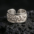 Load image into Gallery viewer, Polished silver skull cuff ring on textured volcanic rock, crisp macro product photo emphasizing clean edges, sharp skull detailing, and bright reflective highlights across the open band.