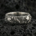 Load image into Gallery viewer, Oxidized skull and koi floral band ring on textured volcanic rock, centered close-up highlighting the raised skull accents, koi scale texture, floral relief, and deep antique shadowed contrast.