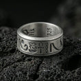 Load image into Gallery viewer, Oxidized Egyptian symbols band ring on textured volcanic rock, centered close-up highlighting the Eye of Horus, ankh motif, engraved glyphs, and deep antique shadowed contrast.