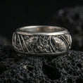 Load image into Gallery viewer, Oxidized koi fish and lotus band ring on textured volcanic rock, centered close-up highlighting the twin koi relief, lotus flower centerpiece, and deep antique shadowed contrast.