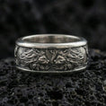Load image into Gallery viewer, Oxidized twin lion band ring on textured volcanic rock, centered close-up highlighting the facing lion heads, flowing mane relief, and deep antique shadowed contrast.