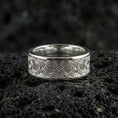Load image into Gallery viewer, Polished silver geometric knotwork band ring on textured volcanic rock, crisp macro product photo emphasizing clean edges, sharp engraved lines, and bright reflective highlights across the band.