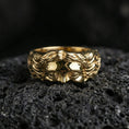 Load image into Gallery viewer, Gold plated face relief band ring on textured volcanic rock, premium close-up with warm reflective shine across the raised face detail and hair texture.