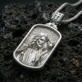 Load image into Gallery viewer, Polished silver Jesus medallion with shepherd motif, lamb detail, and rounded rectangular frame placed on textured volcanic rock in a premium studio product shot