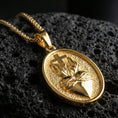 Load image into Gallery viewer, Gold plated Sacred Heart pendant with cross detail, wrapped heart design, and refined religious symbolism showcased on black volcanic rock in a refined macro jewelry image