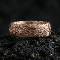 Load image into Gallery viewer, Rose gold plated scrollwork band ring on volcanic stone, refined close-up featuring soft rose highlights and ornate swirling pattern depth.