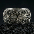Load image into Gallery viewer, Oxidized sterling silver ornate cross band ring on volcanic stone, macro close-up highlighting deep relief scrollwork and antique contrast around the cross motif.