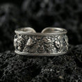 Load image into Gallery viewer, Oxidized sterling silver mythic faces cuff band ring on volcanic stone, macro close-up highlighting deep relief character details and antique contrast.